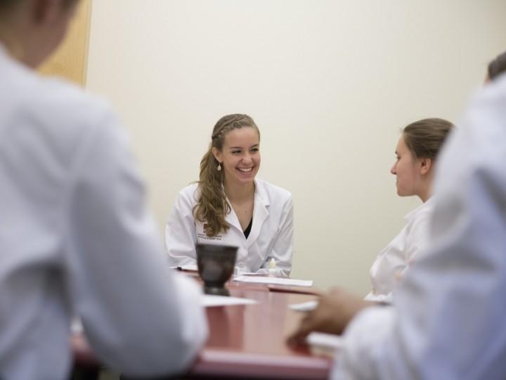 Students sitting around the table in white coats during lab coursework